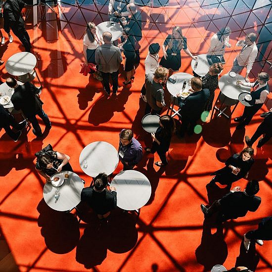 Ansicht von oben in das Forum der AXICA Eventlocation, Stehtische auf rotem Teppich mit sich unterhaltenden Menschen beim Empfang einer Veranstaltung